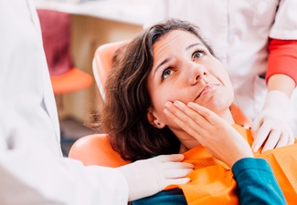 Woman in the dental chair touching her cheek 