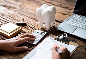 a person looking over a dental invoice while using a calculator with their other hand