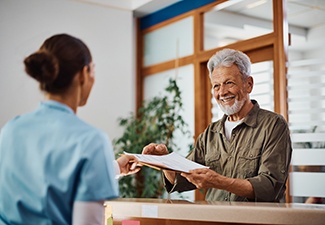 a man handing his paperwork to a dental assistant