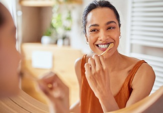 a woman brushing her teeth and looking in a bathroom mirror