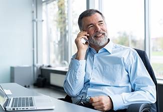 Older man with dental implants in Leawood using a phone