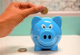 Close up of a hand putting coin in blue piggy bank