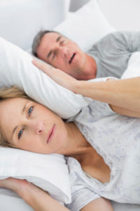 Tired wife blocking her ears from noise of husband snoring