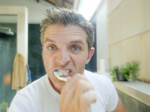 man brushing his teeth aggressively 